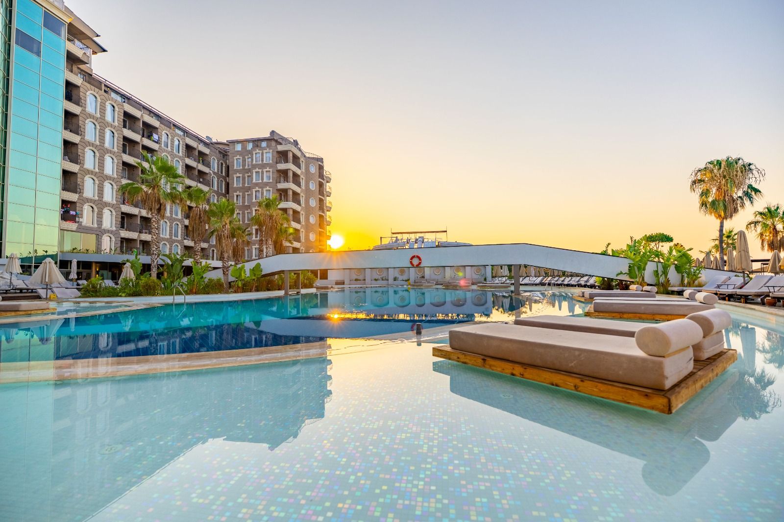 Luxury resort pool with floating loungers and palm trees at sunset