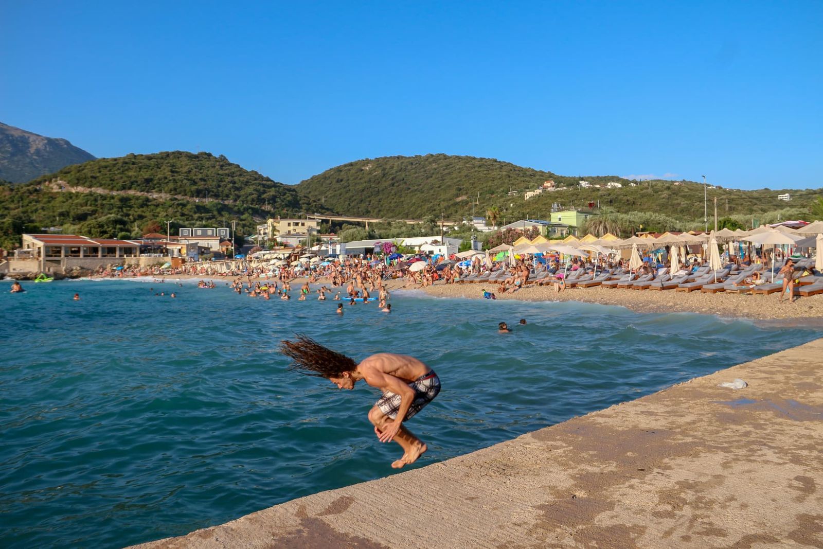 Young man somersaulting off a pier into turquoise water